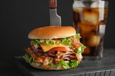 Photo of Tasty burger with bacon and cola served on board, closeup