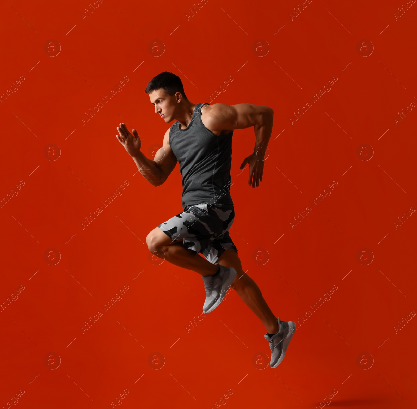 Photo of Athletic young man running on red background, side view