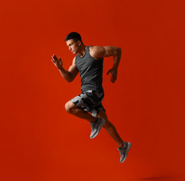 Photo of Athletic young man running on red background, side view