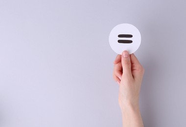 Photo of Woman holding equals sign on light background, closeup. Space for text