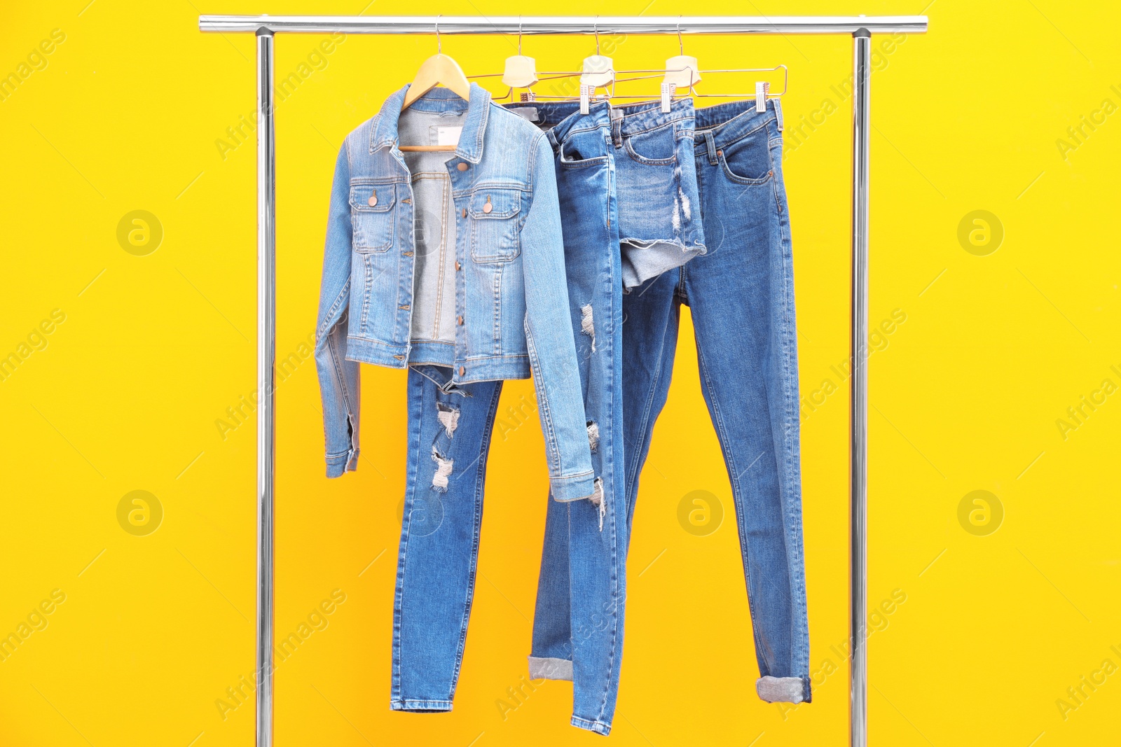 Photo of Rack with stylish jeans and denim clothes on color background