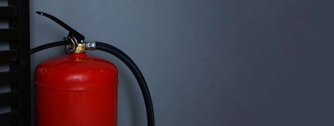 Fire extinguisher near grey wall indoors, space for text. Banner design