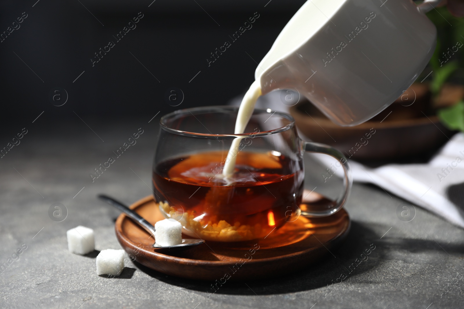 Photo of Pouring milk into cup of tea on grey table, closeup