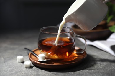 Photo of Pouring milk into cup of tea on grey table, closeup