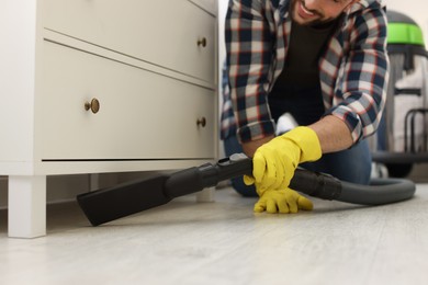 Photo of Man vacuuming floor under chest of drawers indoors, closeup