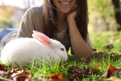 Photo of Happy woman with cute white rabbit on grass in park, closeup