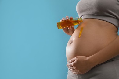 Pregnant woman applying cosmetic product on belly against light blue background, closeup. Space for text