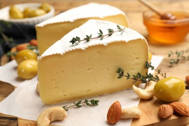 Photo of Tasty Camembert cheese with thyme, olives and nuts on wooden table, closeup
