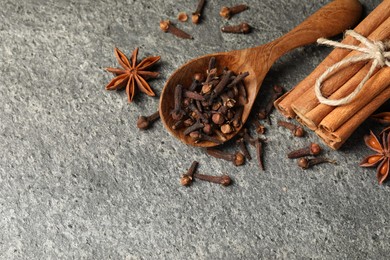 Wooden spoon with different spices on gray textured table, flat lay. Space for text