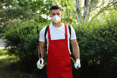 Photo of Worker with insecticide sprayer near green bush outdoors. Pest control