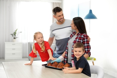 Happy family with tray of oven baked buns in kitchen