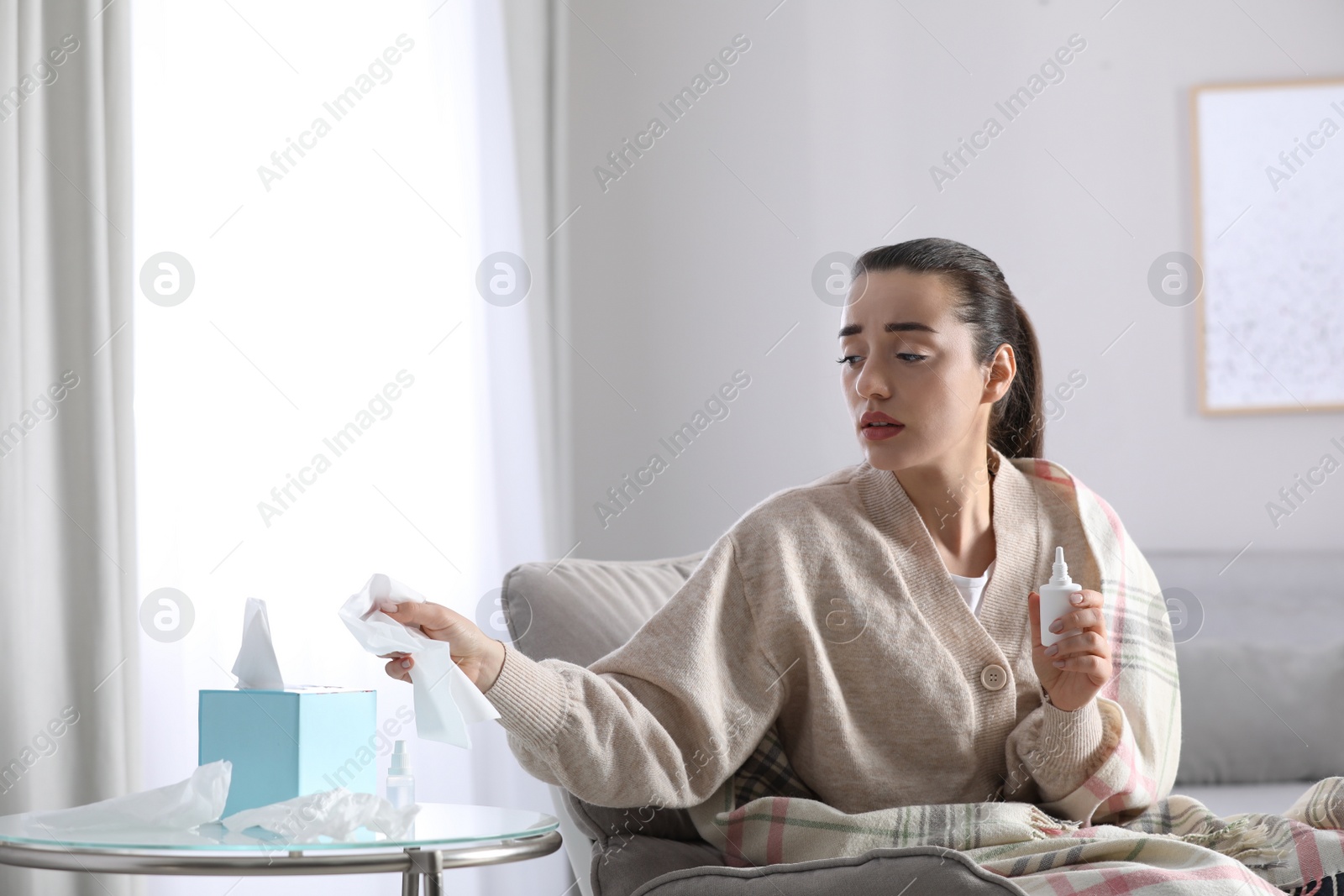 Photo of Sick young woman with napkins and nasal spray at home