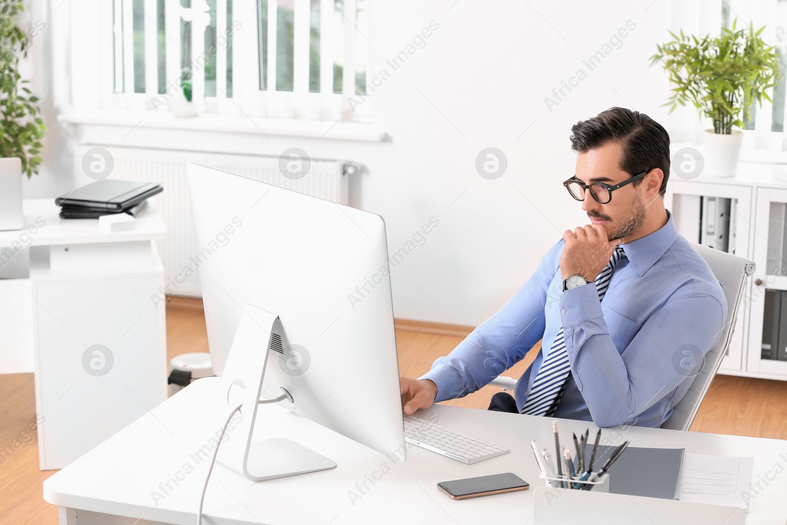 Photo of Handsome young man working with computer at table in office