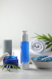 Photo of Spa composition. Cosmetic products, sea salt, towels and burning candle on light table, space for text