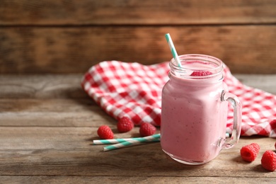 Image of Yummy raspberry smoothie in mason jar on wooden table. Space for text