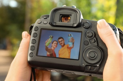 Photo of Female photographer holding professional camera with picture on screen outdoors, closeup