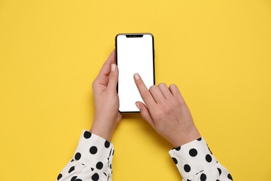 Woman using smartphone on yellow background, top view