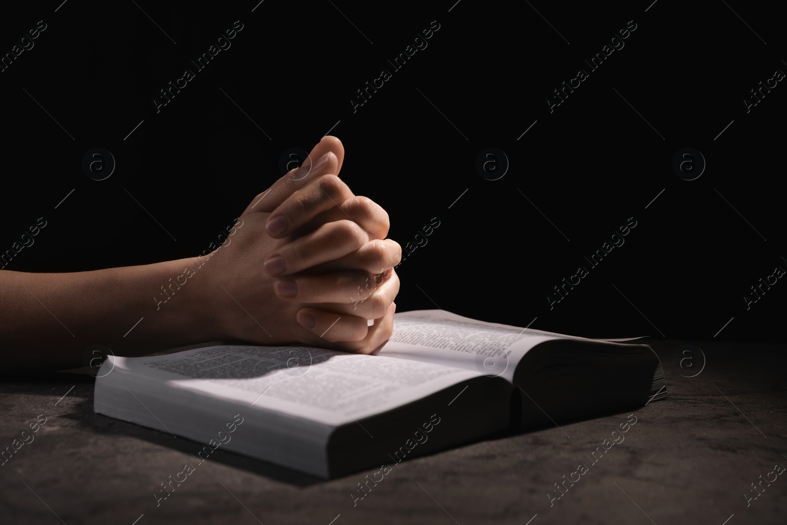 Photo of Religion. Christian woman praying over Bible at table against black background, closeup. Space for text