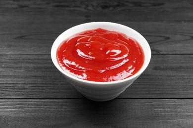 Photo of Delicious ketchup in bowl on black wooden table, closeup. Tomato sauce