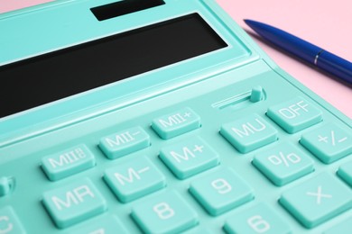 Calculator and pen on pink background, closeup