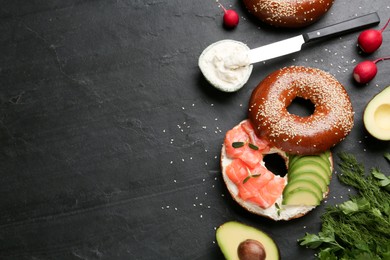 Delicious bagel with cream cheese, salmon and avocado on black table, flat lay. Space for text