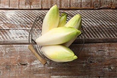 Fresh raw Belgian endives (chicory) in metal basket on wooden table, top view