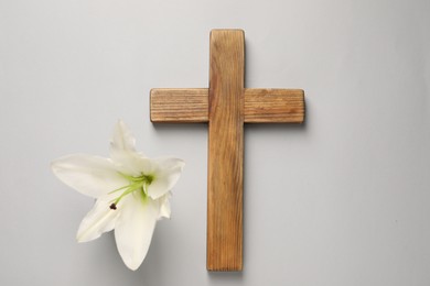 Photo of Wooden cross and lily flower on grey background, top view. Easter attributes