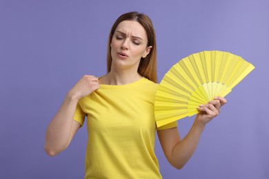 Photo of Beautiful woman waving yellow hand fan to cool herself on violet background