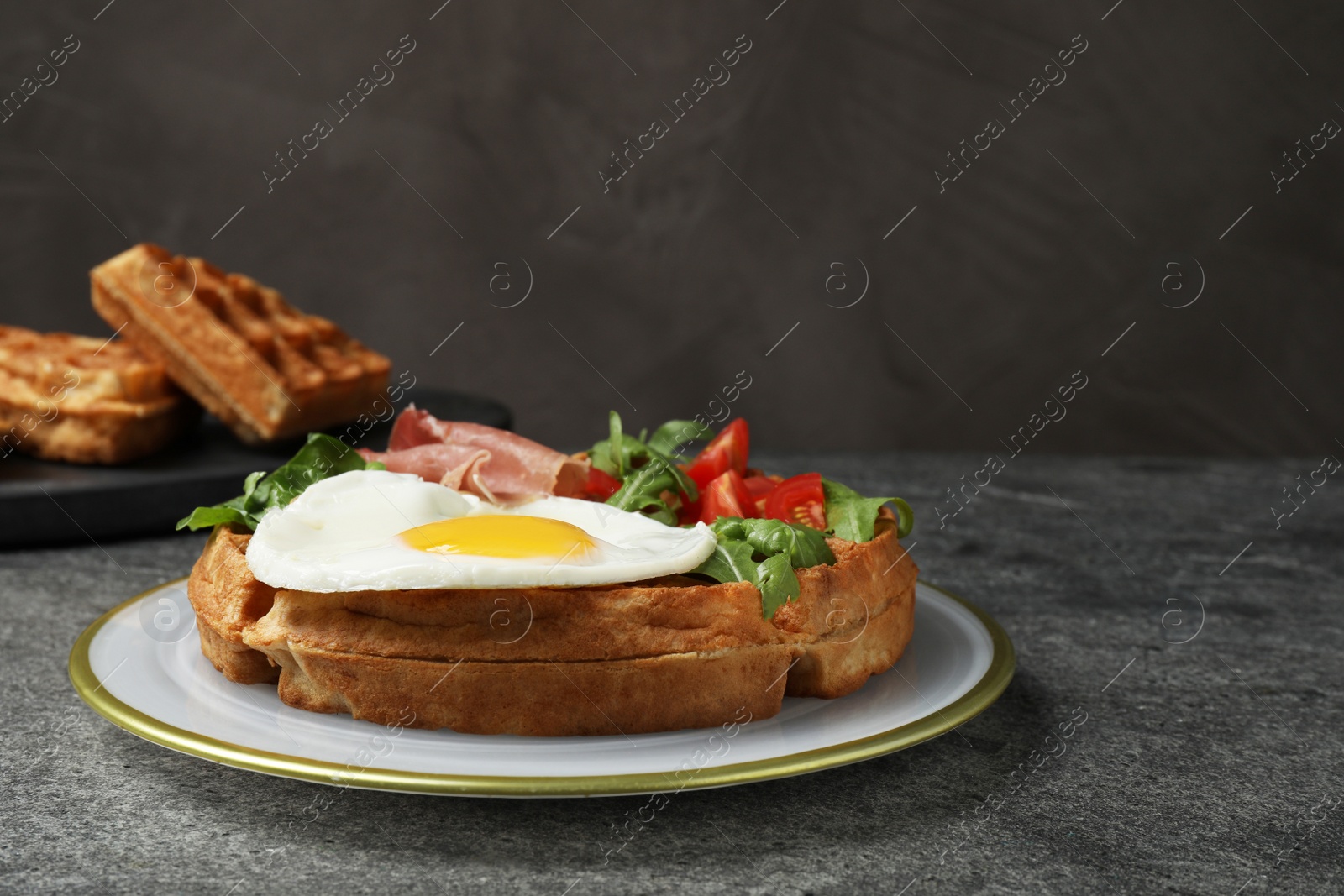 Photo of Fresh Belgian waffle with fried egg, arugula, tomatoes and jamon served for breakfast on grey table