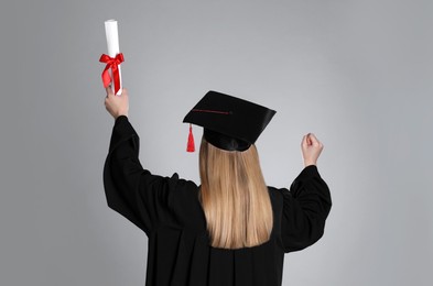 Student with diploma on grey background, back view