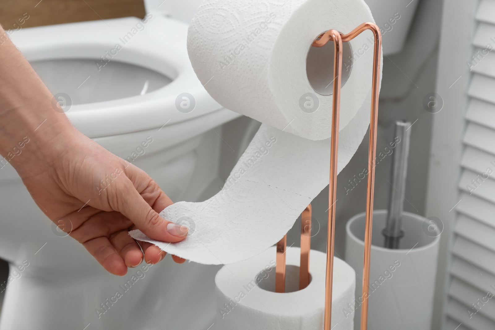 Photo of Woman taking toilet paper from roll holder in bathroom, closeup