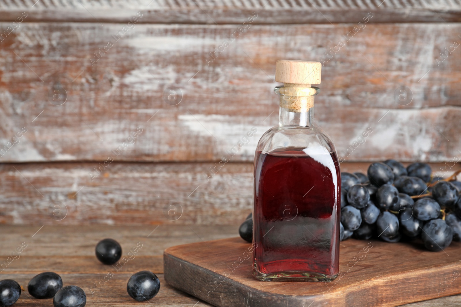 Photo of Glass bottle with wine vinegar and fresh grapes on wooden table. Space for text