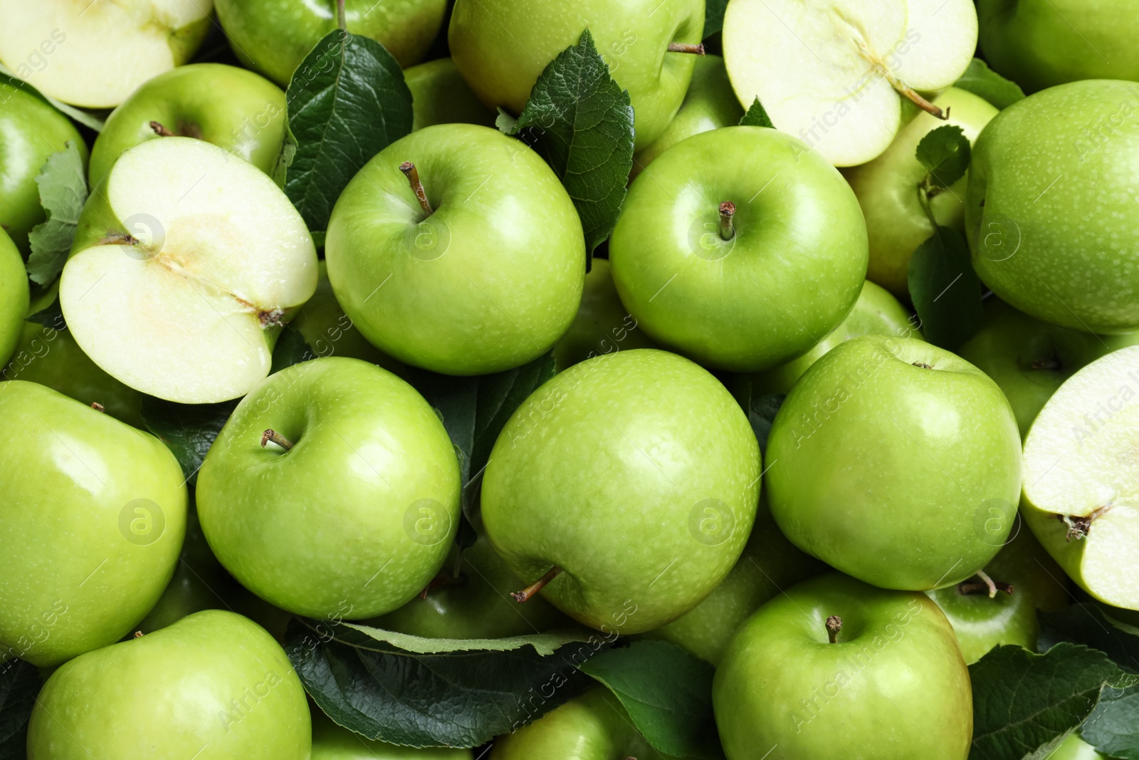 Photo of Pile of tasty green apples with leaves as background, top view