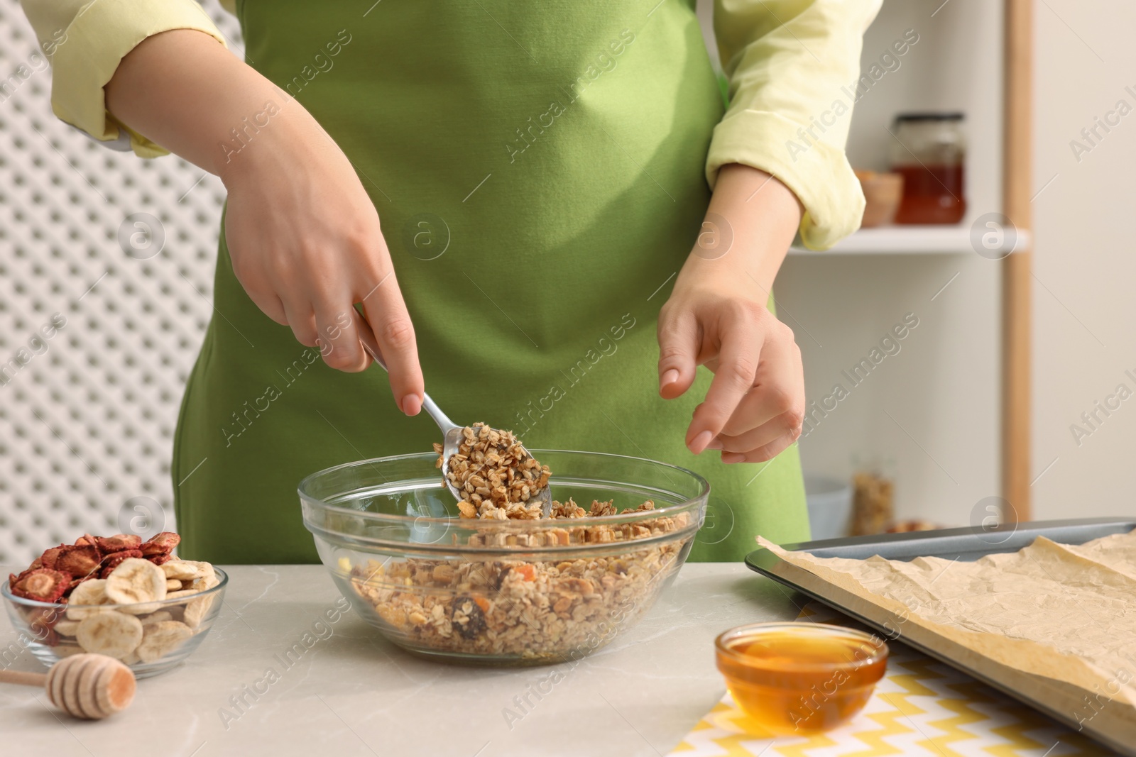 Photo of Woman making granola at light marble table in kitchen, closeup