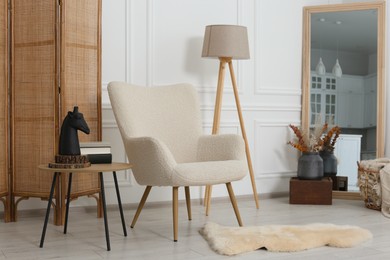 Photo of Stylish beige armchair, small coffee table and mirror in living room. Interior design