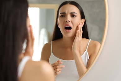 Photo of Suffering from allergy. Emotional young woman looking at her irritated skin near mirror indoors