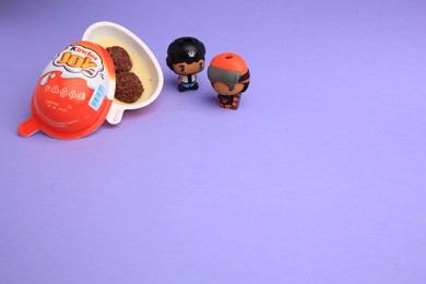Photo of Sveti Vlas, Bulgaria - June 30, 2023: Kinder Joy Egg with sweet candies and toys on violet background, space for text