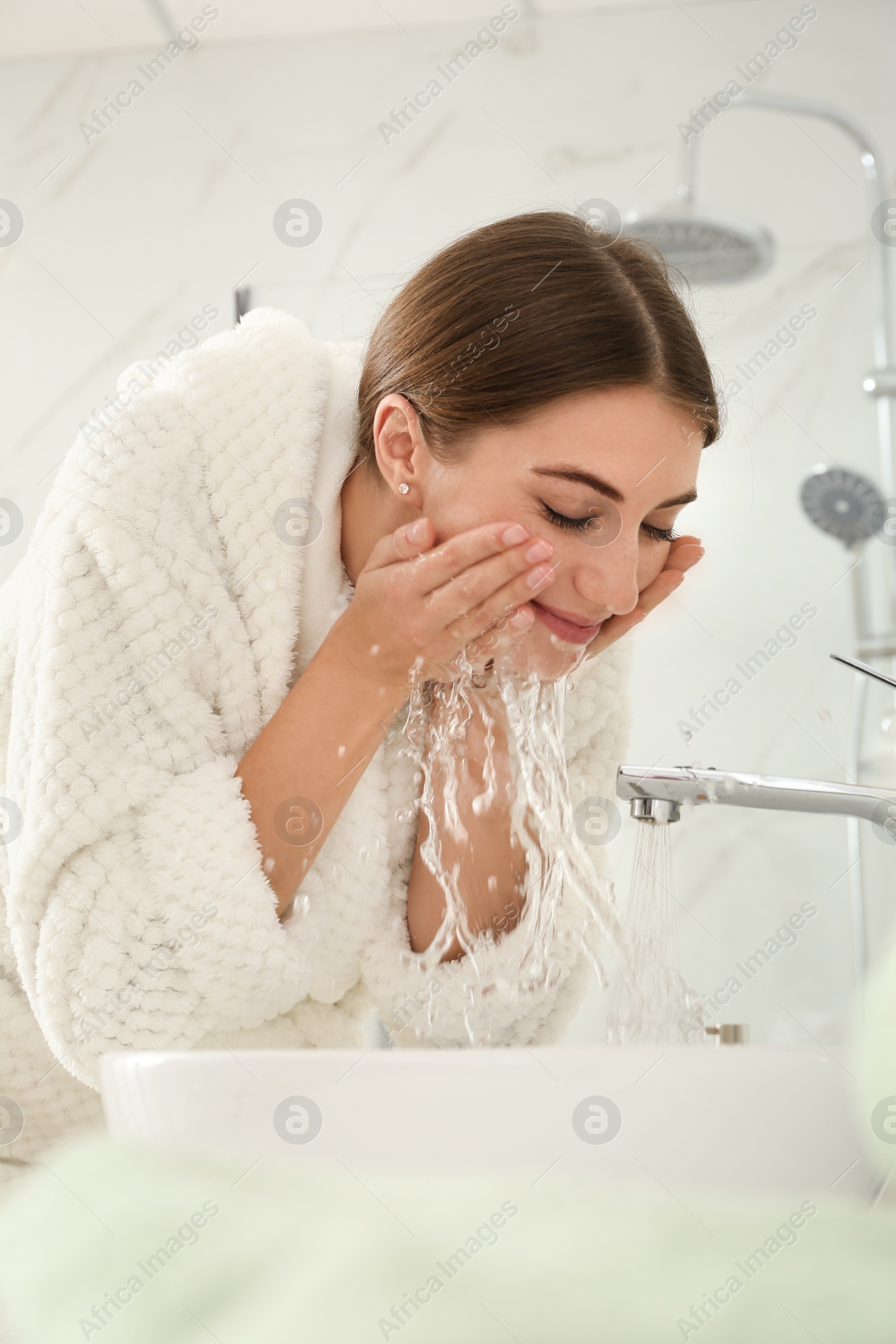 Photo of Young woman washing her face with water in bathroom