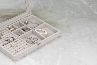 Photo of Jewelry box with many different accessories on light grey table. Space for text