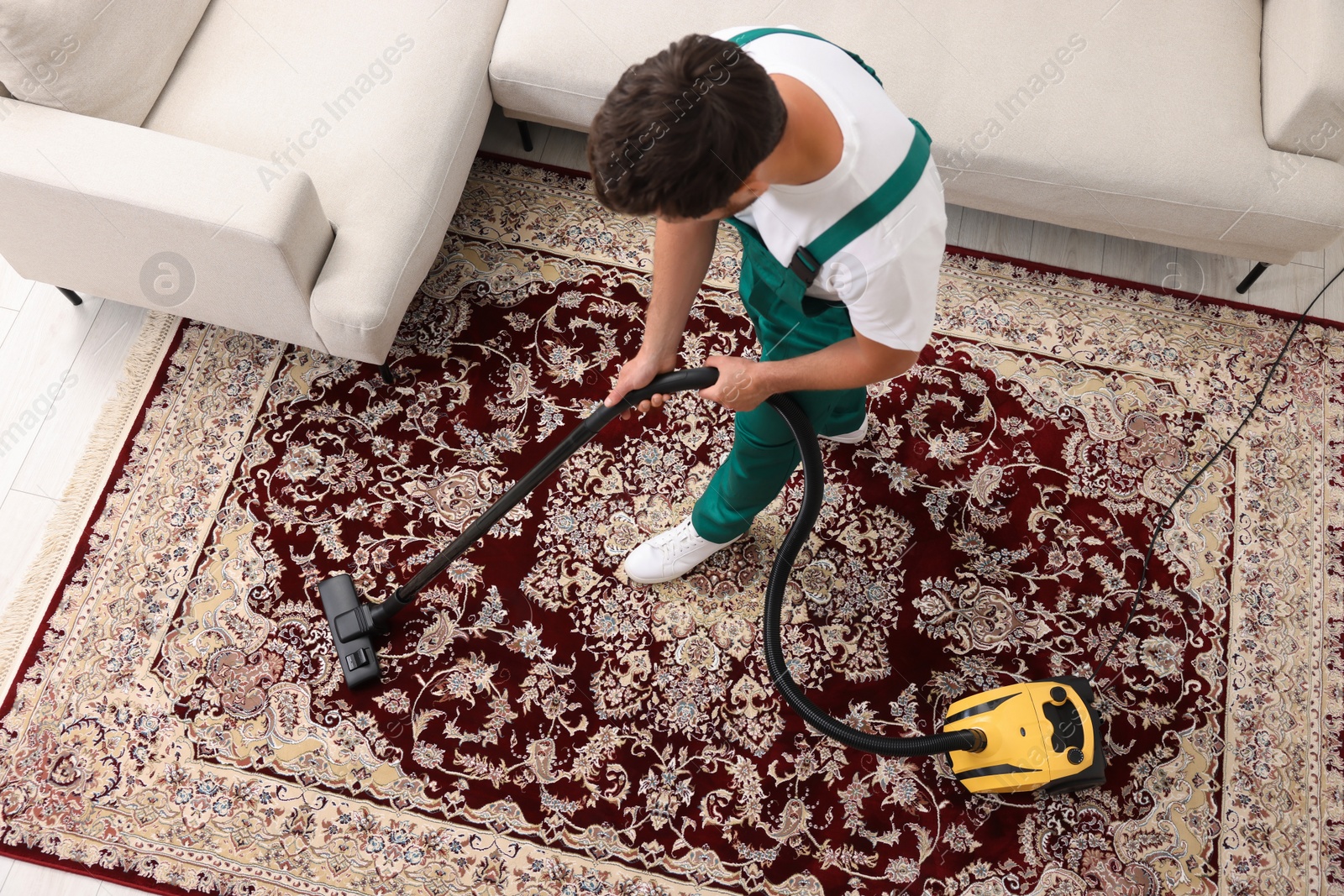 Photo of Dry cleaner's employee hoovering carpet with vacuum cleaner indoors, above view