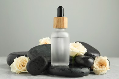 Photo of Bottle of face serum with spa stones and beautiful roses on wet table against grey background, closeup