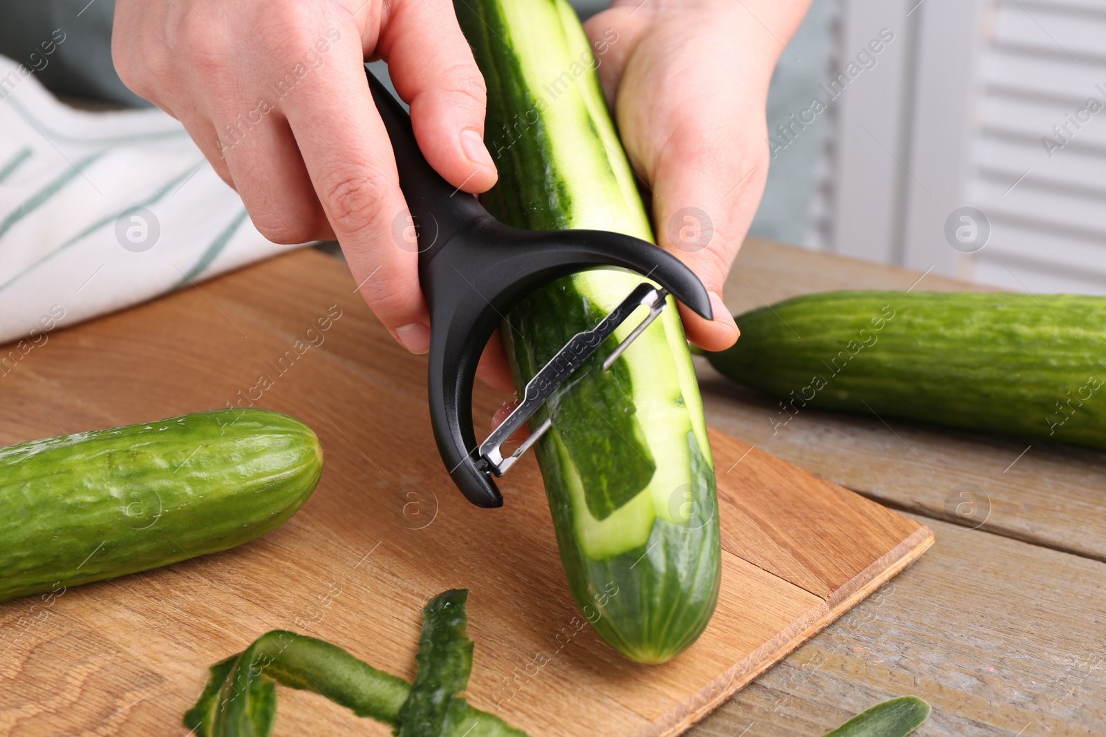 Photo of Woman peeling cucumber at wooden table indoors, closeup