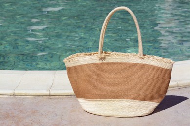 Photo of Stylish bag near outdoor swimming pool on sunny day, space for text. Beach accessory