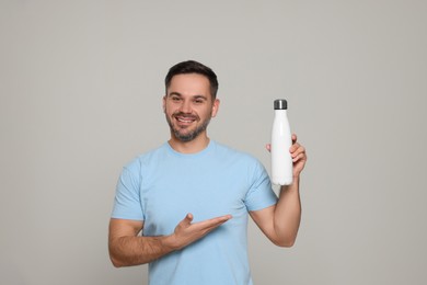 Photo of Happy man showing thermo bottle on light grey background