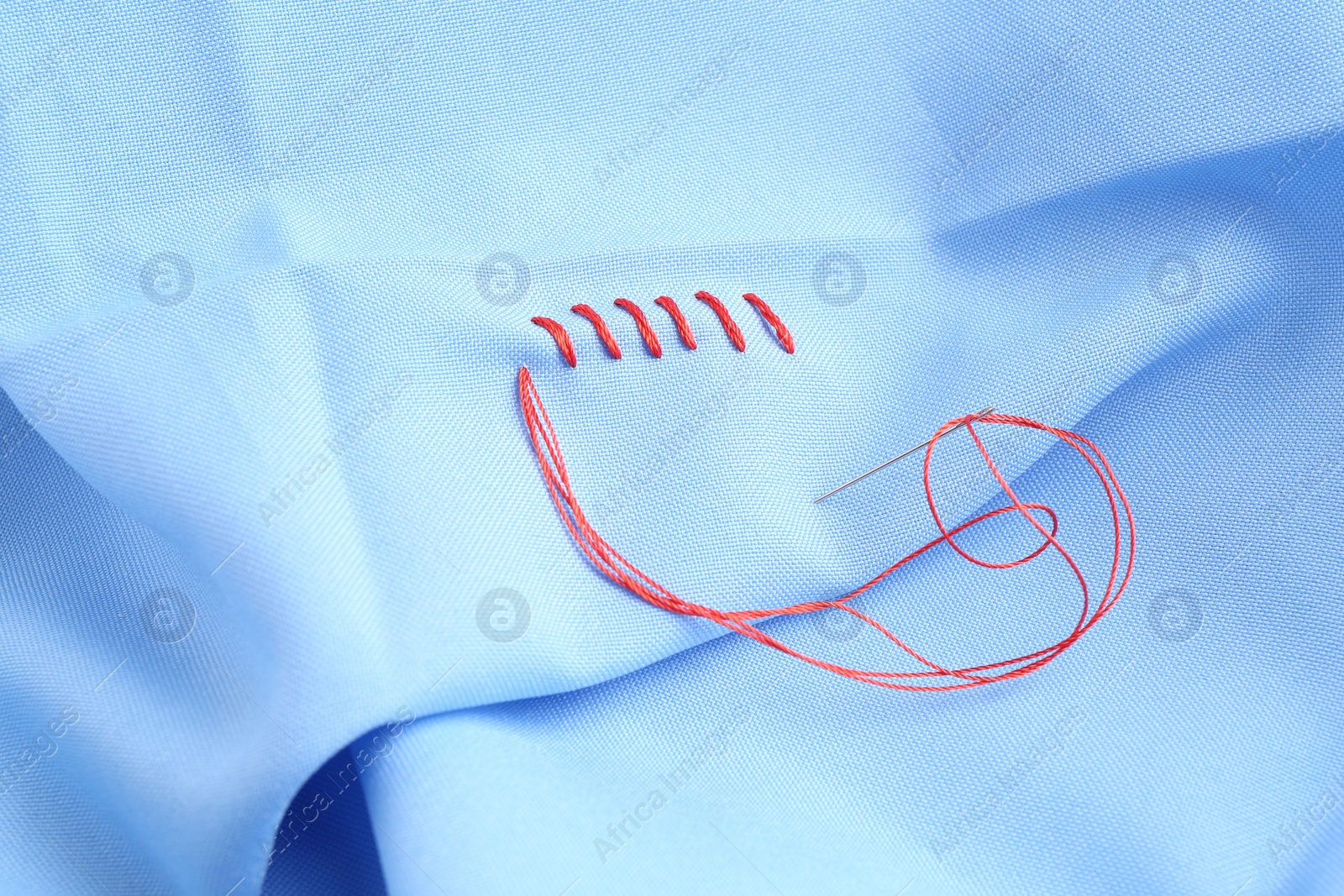 Photo of Sewing needle with thread and stitches on light blue cloth, closeup