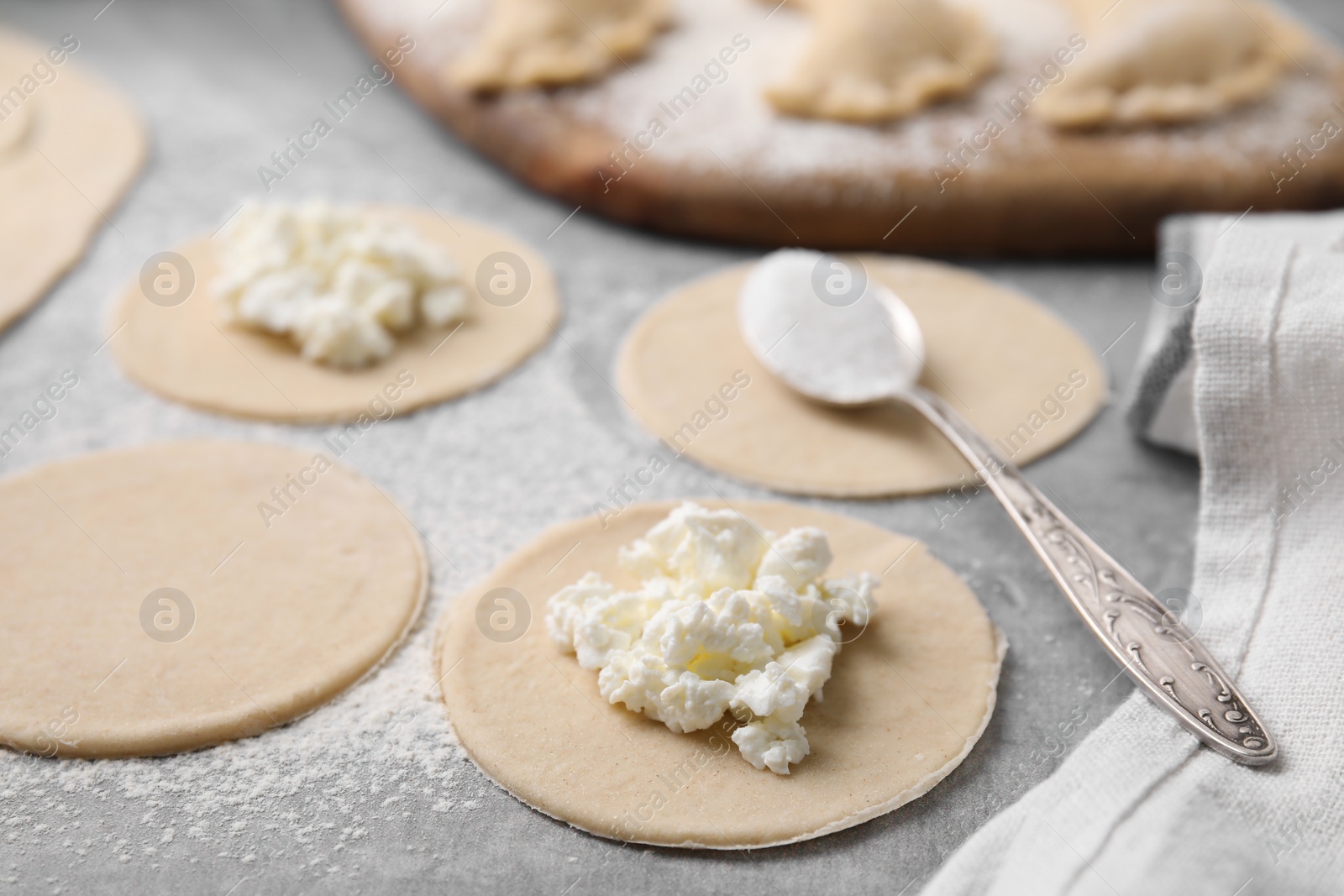 Photo of Process of making dumplings (varenyky) with cottage cheese. Raw dough and ingredients on grey table, closeup