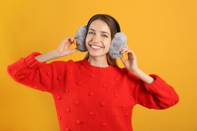 Photo of Happy woman wearing warm earmuffs on yellow background