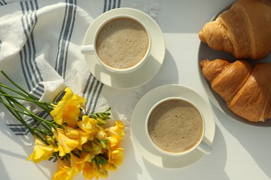 Photo of Coffee, croissants, flowers and card with phrase GOOD MORNING! on white wooden table, flat lay