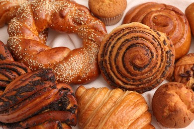 Photo of Different tasty freshly baked pastries on white tablecloth, flat lay