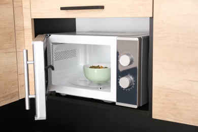 Open modern microwave oven with dish in kitchen